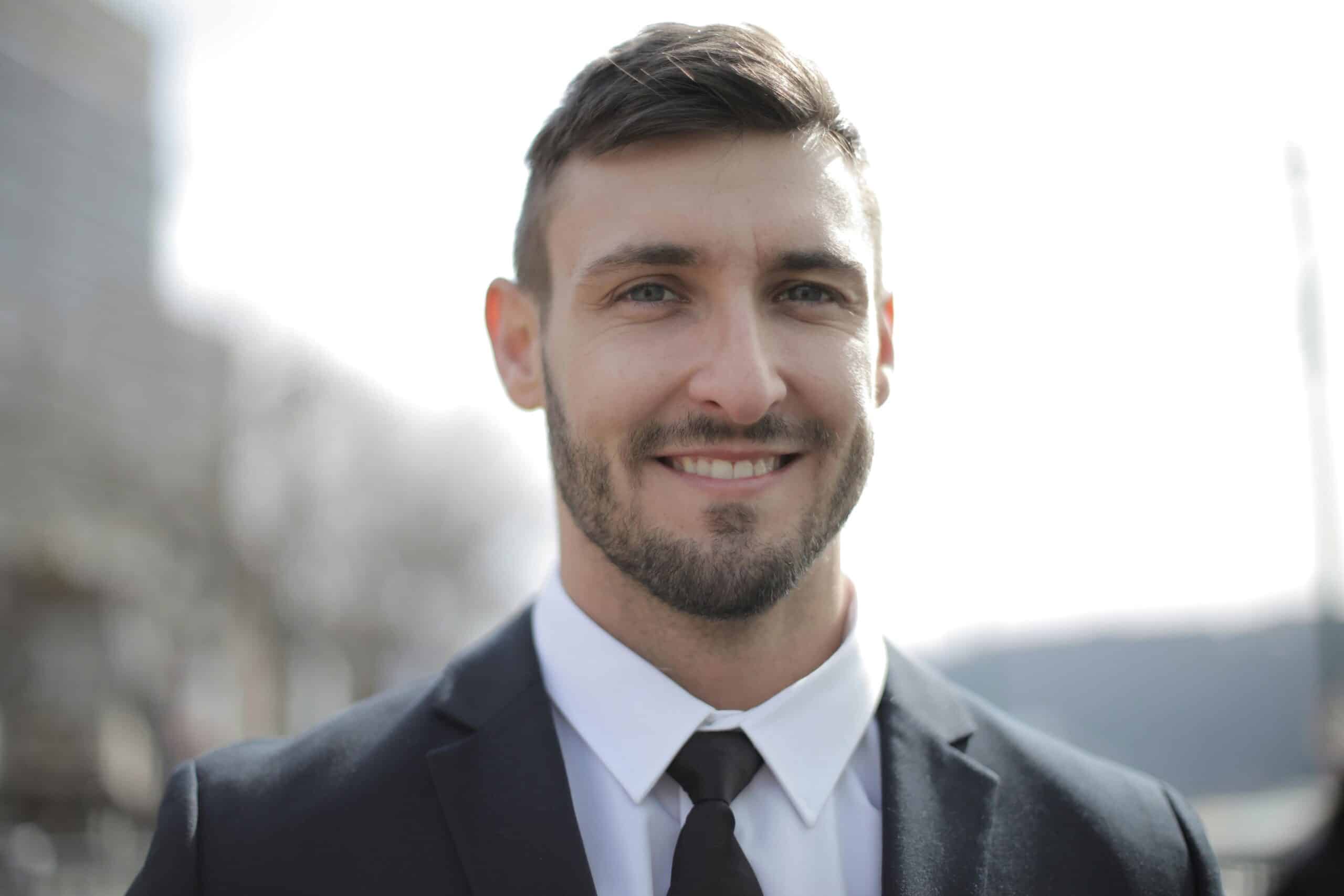 A smiling businessman in a suit standing outdoors with a bright expression.